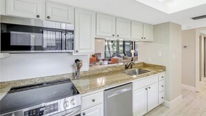 Una cocina moderna con armarios blancos, encimera de granito, estufa integrada y lavavajillas.