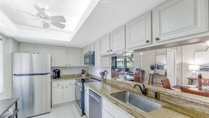 Una cocina moderna con gabinetes blancos, electrodomésticos de acero inoxidable, encimeras de granito y un ventanal amplio.