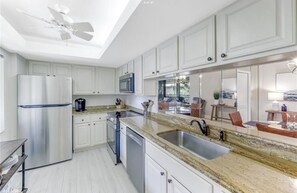 A modern kitchen with white cabinets, stainless steel appliances, granite countertops, and a large window. - NEW on VRBO! Exclusive Bonita Bay Resort style living. 2 Bed, 2 Bath condo. (Bonita Springs)