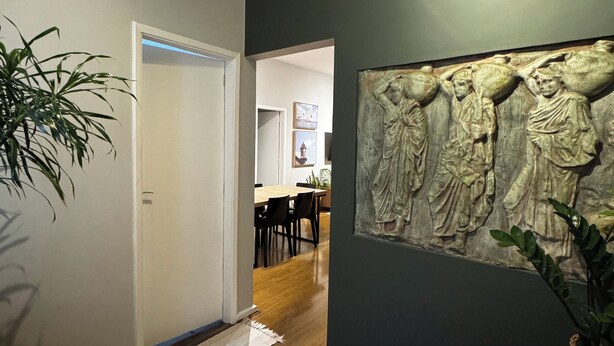 A hallway with a wooden floor, a dark wall with a relief sculpture, and a door leading to a dining area. - Leblon Penthouse: Everything within walking distance! (Rio de Janeiro)