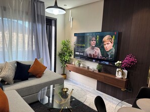 A modern living room with a sofa, a glass coffee table, and a flat-screen TV mounted on the wall. - Studio Stadium Oasis Casablanca (Casablanca)