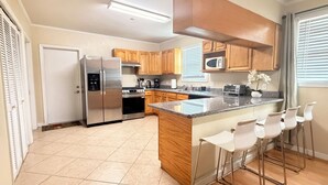 A modern kitchen with a stainless steel refrigerator, wooden cabinets, a granite countertop, and a bar stool seating area.