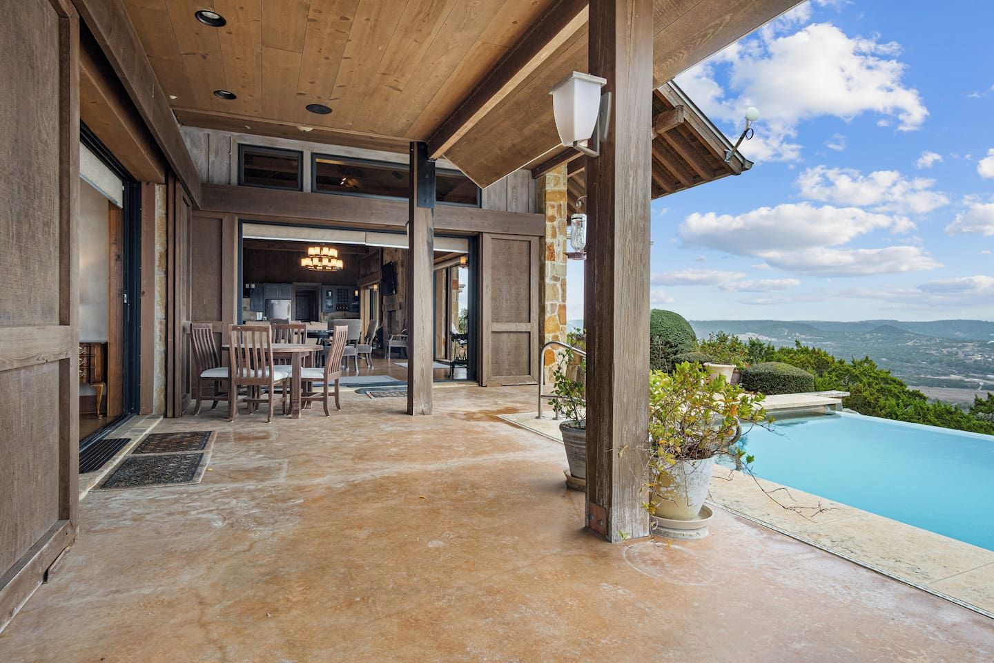 A spacious outdoor area with a pool, wooden furniture, and a view of the landscape.