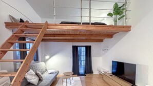 A loft-style living room with a wooden staircase, a sofa, a TV, and a plant.