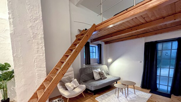 A loft-style living space with a wooden staircase, a grey sofa, a small round table, and a white rug.