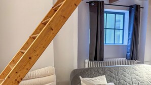 A loft bedroom with a wooden ladder, a grey sofa, and a white armchair.