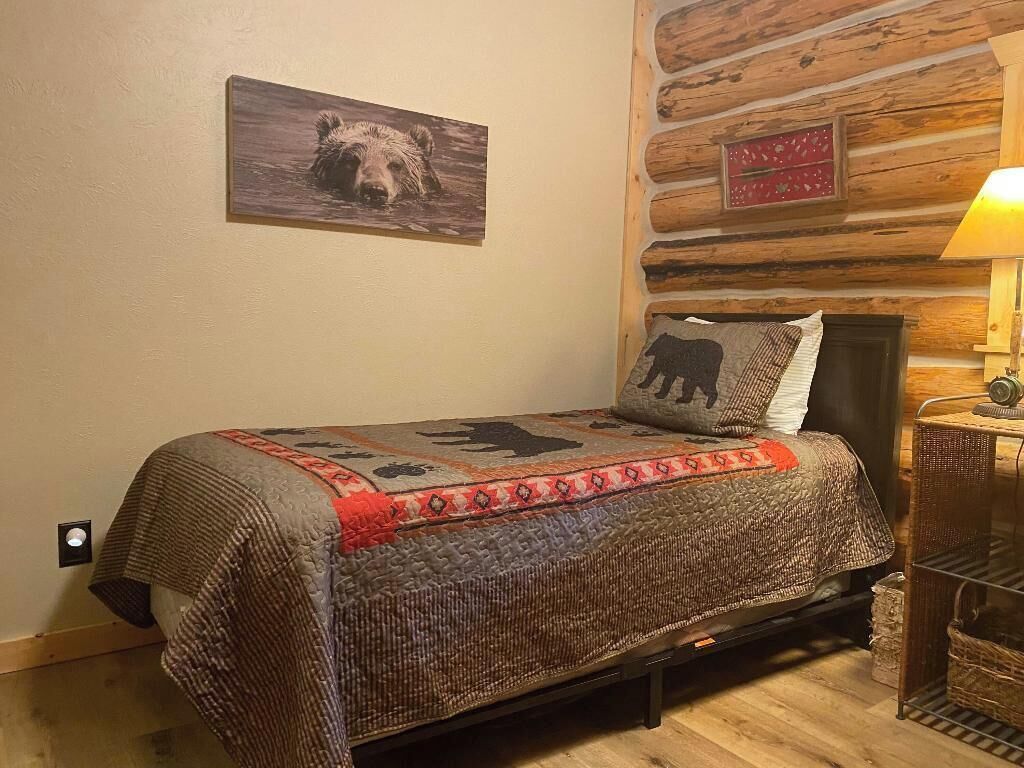A cozy room with a bed, a wooden wall, a lamp, and a bear-themed pillow.