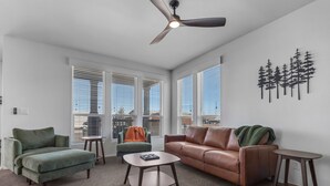 A modern living room with a green armchair, a brown leather sofa, a coffee table, and a ceiling fan. - New KBed 2-bedroom 2 Bath House with Fire Pit in Williams, Grand Canyon, Rt 66 (Williams)
