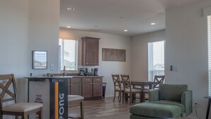 A modern living room with a green sofa, wooden chairs, a coffee table, and a kitchen area with wooden cabinets and a ping pong table. - New KBed 2-bedroom 2 Bath House with Fire Pit in Williams, Grand Canyon, Rt 66 (Williams)