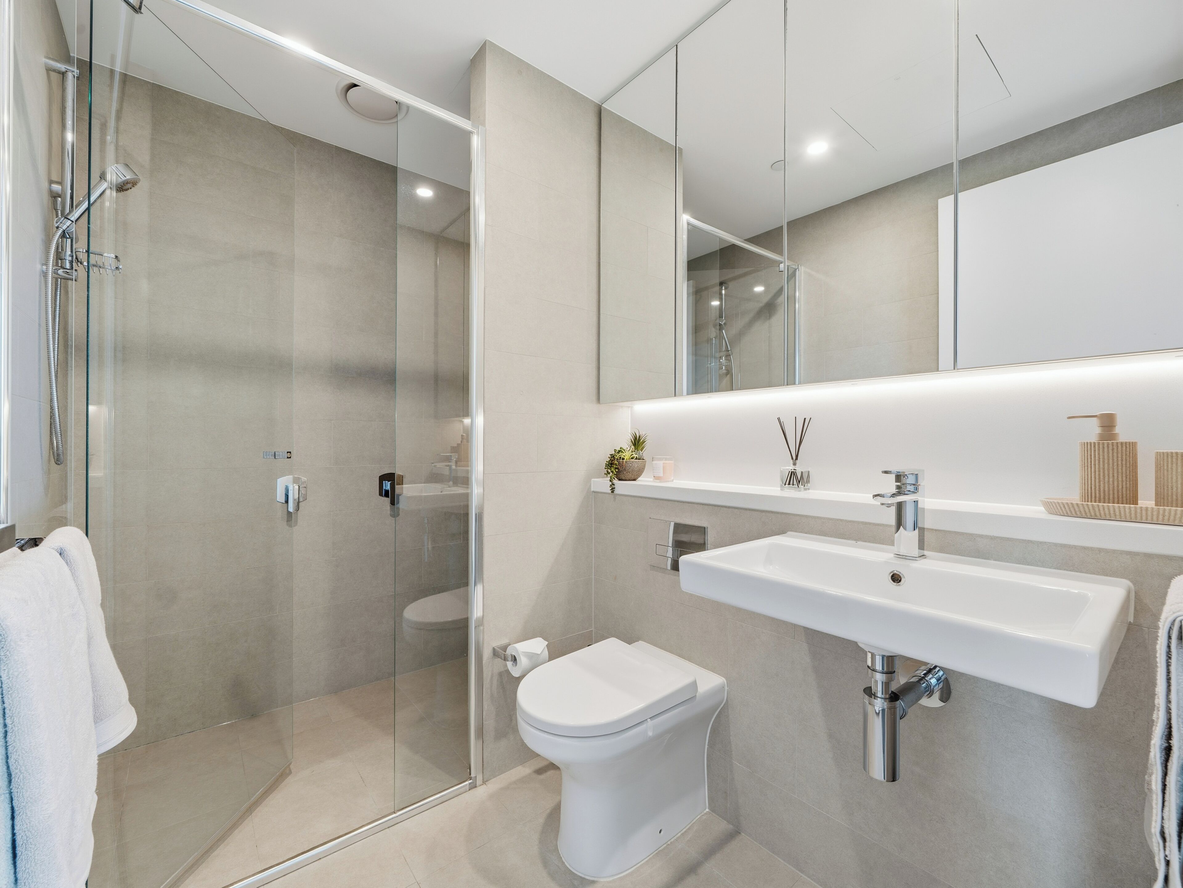 A modern bathroom with a glass-enclosed shower, a white toilet, and a large sink with a mirror above it.