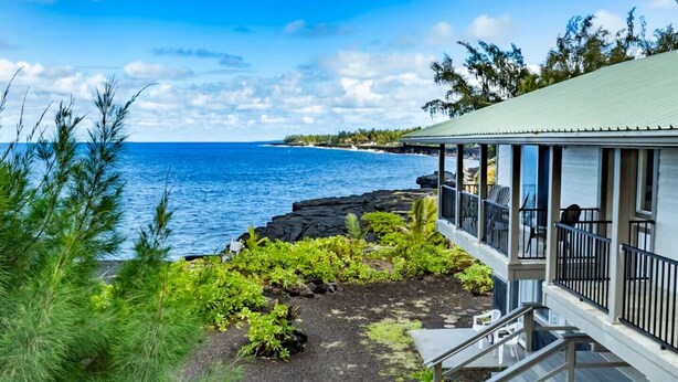 En kystbygning med balkon med udsigt over havet, omgivet af vegetation og vulkansten.