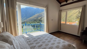 Une chambre avec un lit, un balcon doté d’une rambarde bleue et une grande fenêtre donnant sur les montagnes.