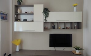 Ein modernes Wohnzimmer mit eingebauten weißen Schränken, einem Flachbildfernseher und Zimmerpflanzen.