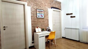 A room with a brick wall, a desk with a chair, a radiator, and a sign that says 'Welcome Home'. - Porta Soprana House, in heart of historic center, bright and close to everything (Genova)
