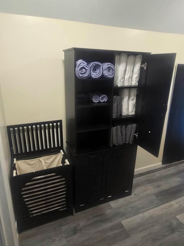 Une armoire noire dotée de nombreuses étagères et d’un espace pour suspendre les vêtements, où sont rangées des serviettes pliées et des vêtements suspendus.