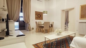 Un salon moderne avec un canapé blanc, une table à manger avec des chaises, une table basse et un tapis à motifs.