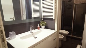 Une salle de bain avec un lavabo blanc, un miroir, des toilettes et un espace douche.
