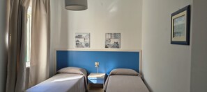 A room with two beds, a desk, a lamp, and two wall art pieces.