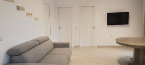A room with a sofa, a dining table, and a TV mounted on the wall. - Spacious apartment in villa with swimming pool (Peschici)