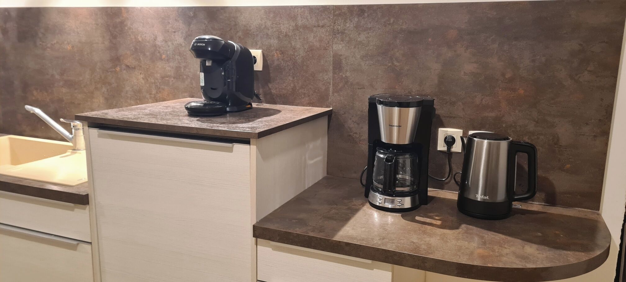 Une cuisine équipée d’une machine à café Bosch, d’une bouilloire Tefal et d’une cafetière Tefal, le tout posé sur le plan de travail.
