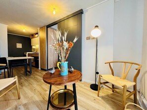 Ein modernes Wohnzimmer mit einem Holzesstisch, einer blauen Vase mit Trockenblumen, einer Stehlampe und einem Holzstuhl.