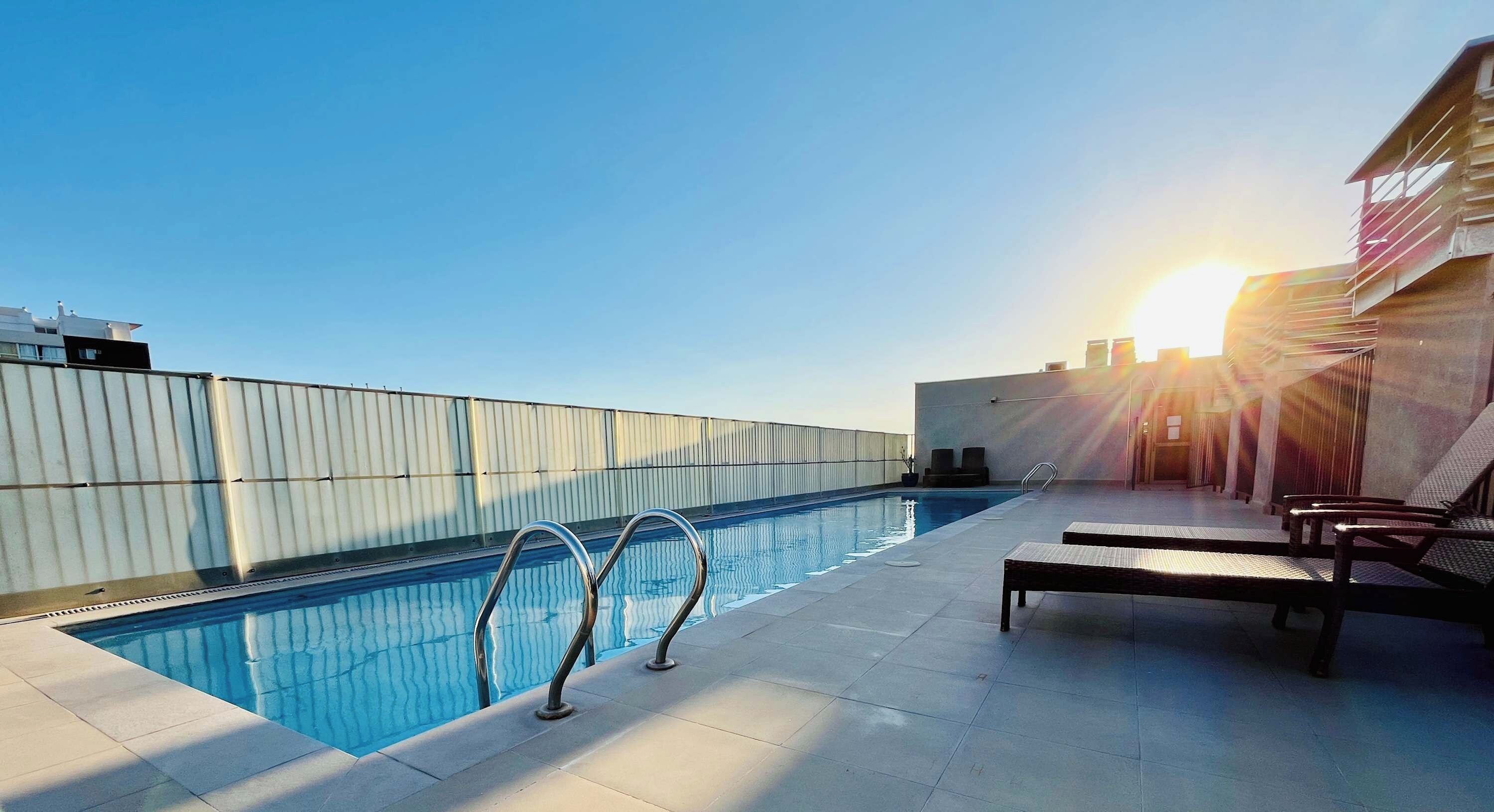 Une piscine sur le toit, avec un ciel dégagé et le soleil couchant en arrière-plan.