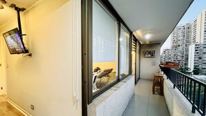 A balcony with a television mounted on the wall, a small table, and a view of high-rise buildings. - Apartment close to Barrio Italia Parking Wifi (Santiago)