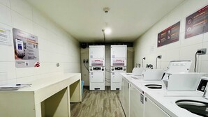 A laundry facility with multiple washing machines and dryers, a counter, and informational posters on the walls. - Apartment close to Barrio Italia Parking Wifi (Santiago)
