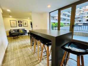 Une cuisine moderne avec un coin bar, un canapé et une table à manger dans un espace de vie donnant sur un bâtiment à l’extérieur.