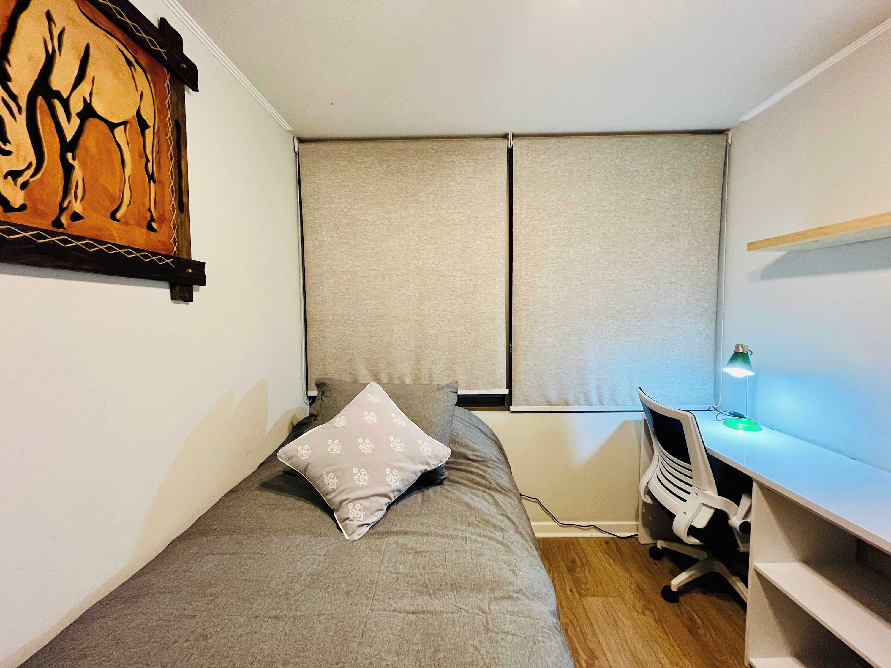 A small, neatly arranged bedroom with a single bed, a desk, and a chair.