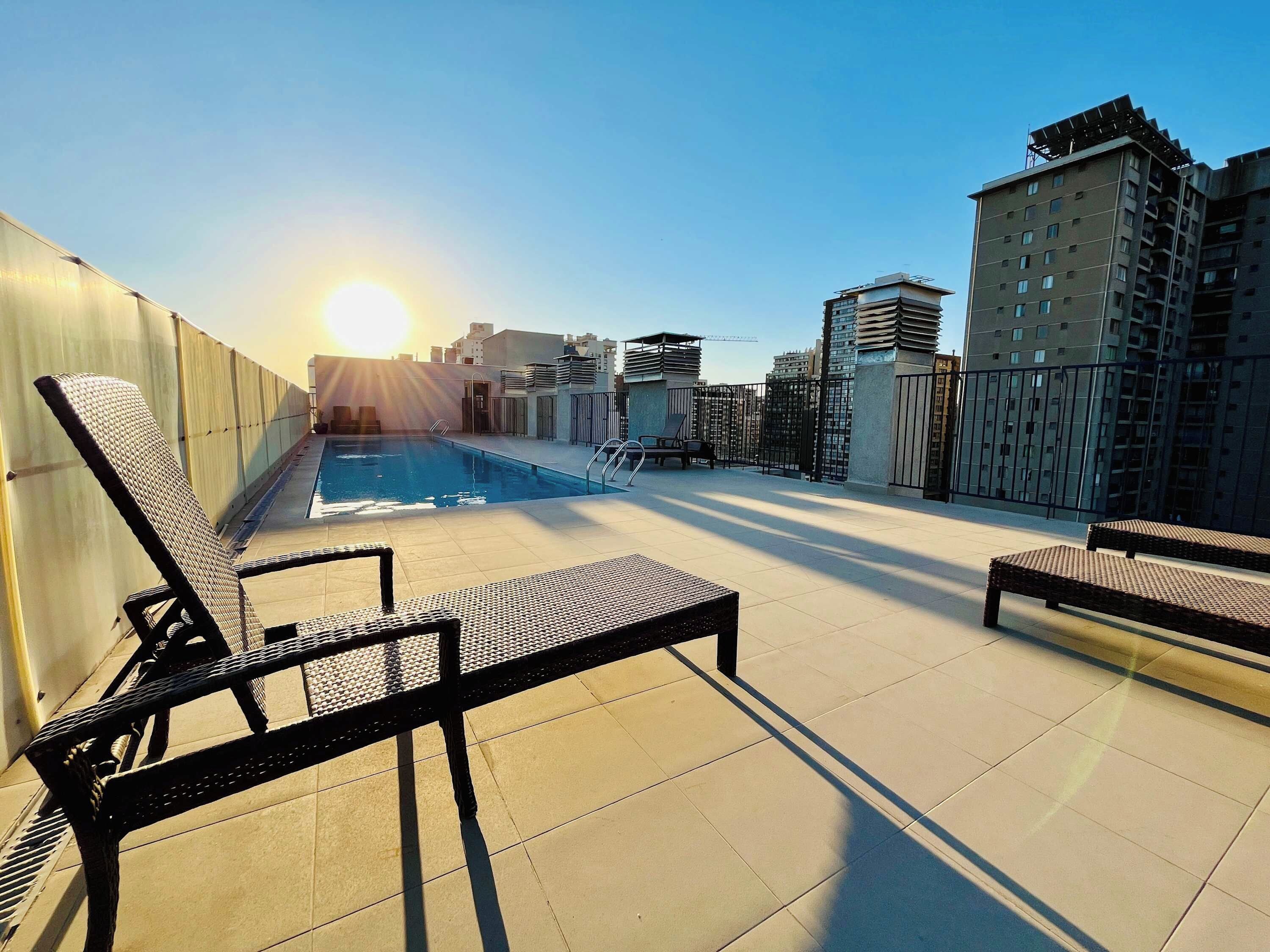 A rooftop pool area with sun loungers and a clear view of the city skyline.