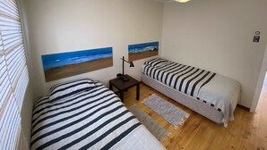 A bedroom with two beds, a nightstand, a lamp, a hanging light fixture, and two wall-mounted paintings.
