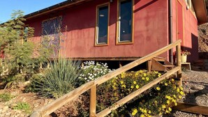 A red building with two windows and a wooden staircase leading up to a door.