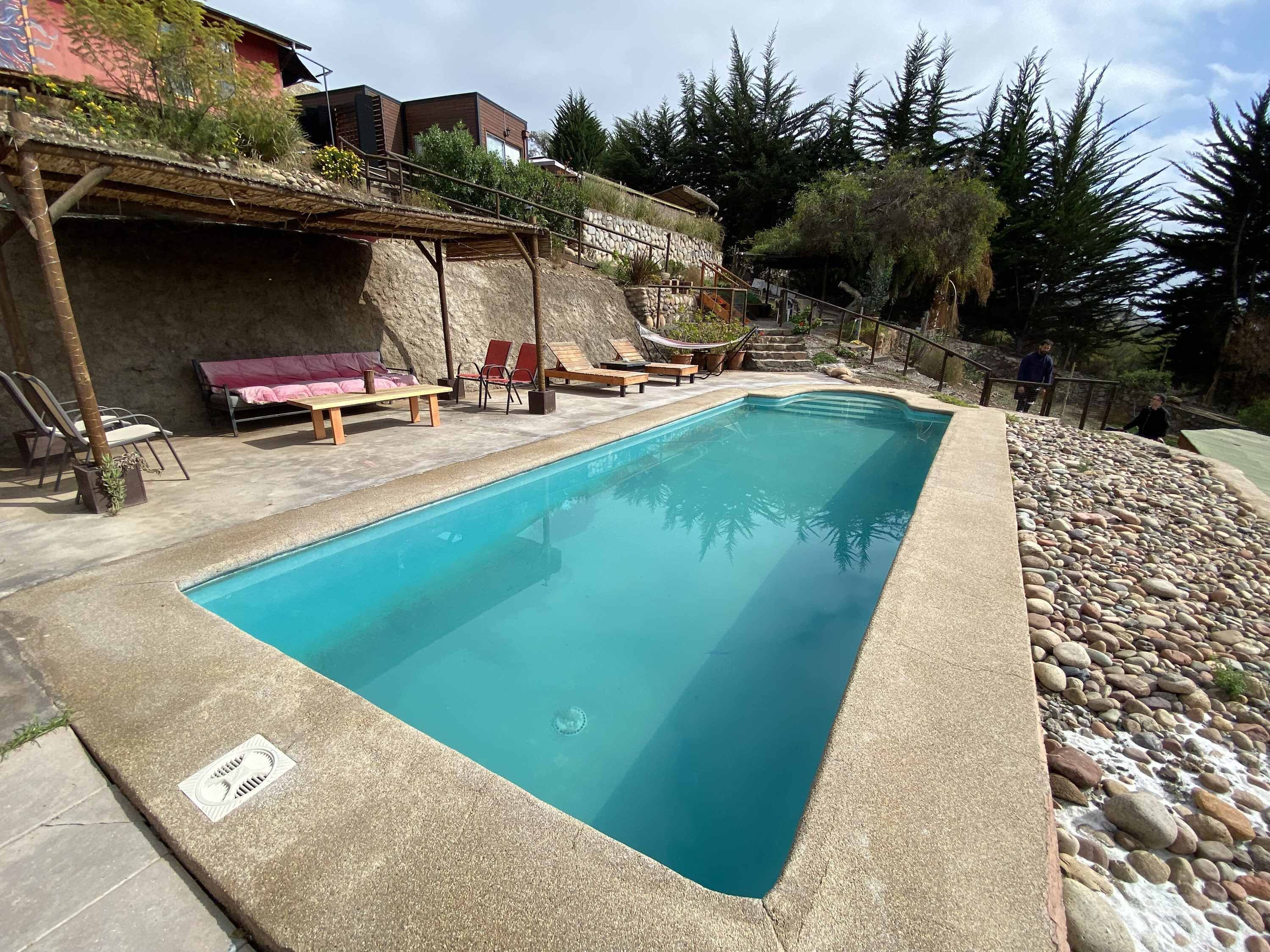 A rectangular swimming pool with a stone edge, surrounded by lounge chairs and a stone wall.