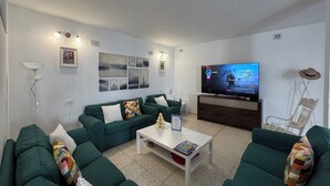 A living room with green sofas, a white coffee table, and a TV on a wooden stand. - Vidamar (Abades)