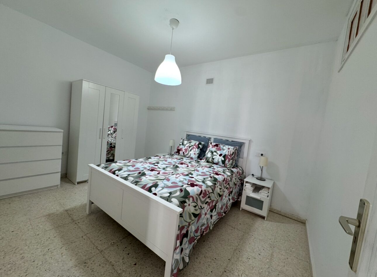 A bedroom with a bed, a wardrobe, a nightstand, and a hanging light fixture.