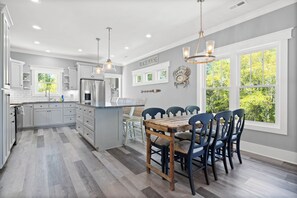 A modern kitchen with a dining area, large windows, and a sign reading 'BEACH HOUSE'. - Oak Haven Getaway - Relax, Unwind & Watch the ICW Drift By (Oak Island)