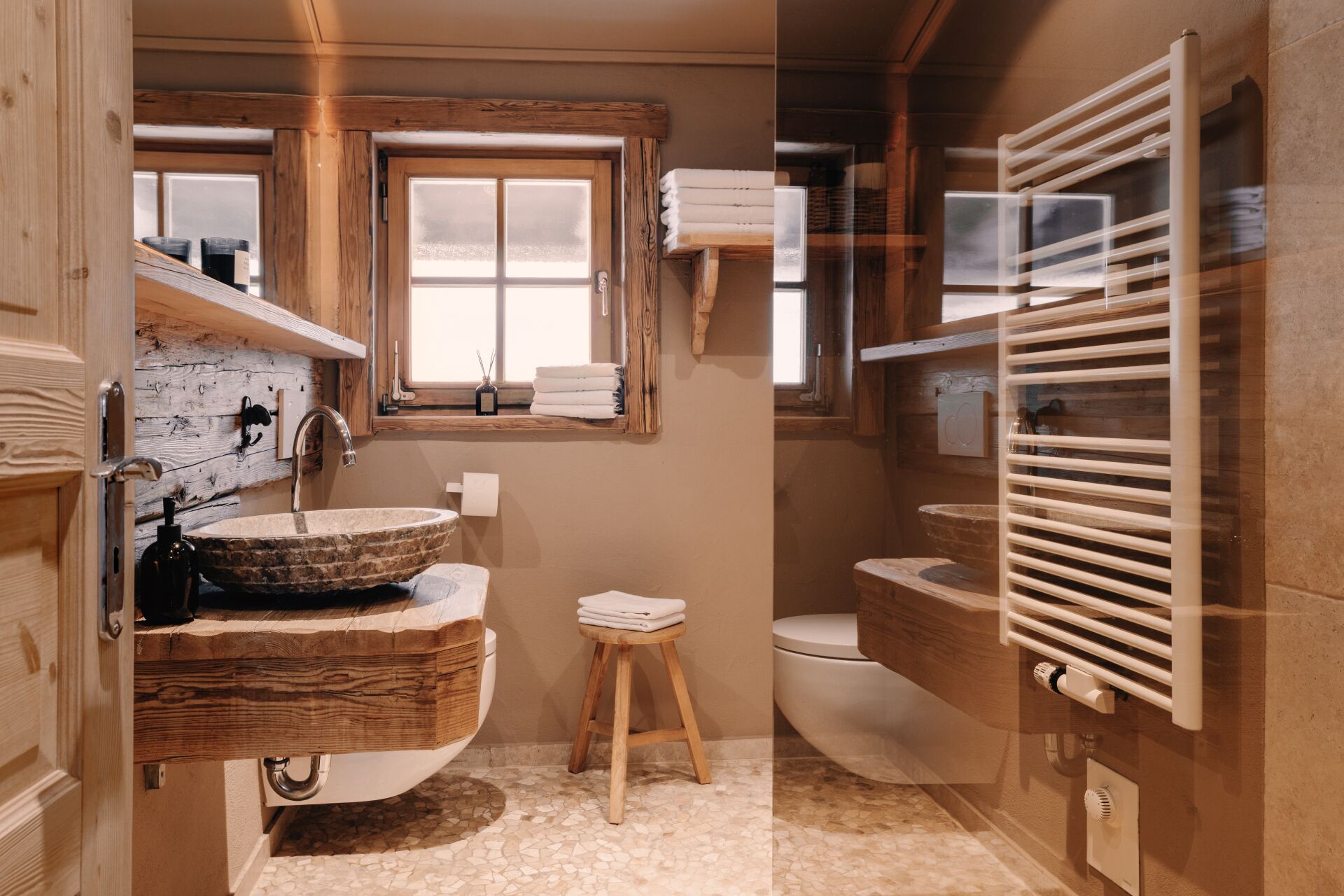 A bathroom with a wooden vanity, a large window, a toilet, and a towel rack.