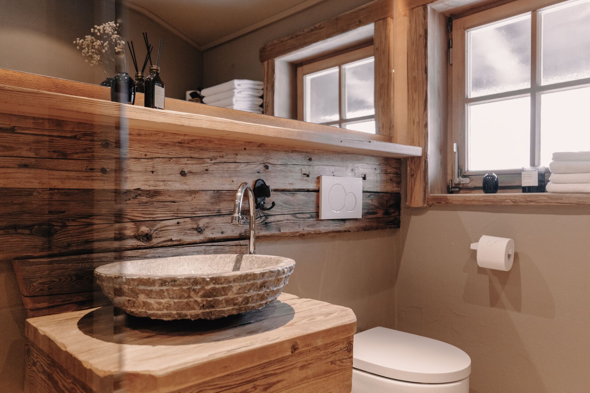 A bathroom with a stone sink, wooden shelves, a toilet, and a window.