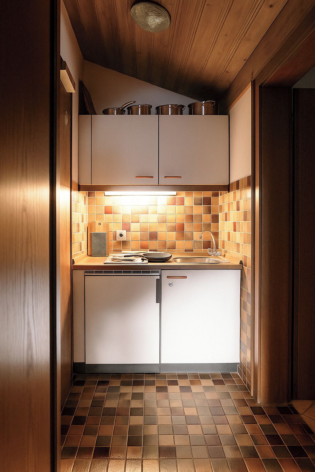 Une cuisine de taille réduite avec des meubles blancs, un pare-feu en carrelage et un plancher en bois.
