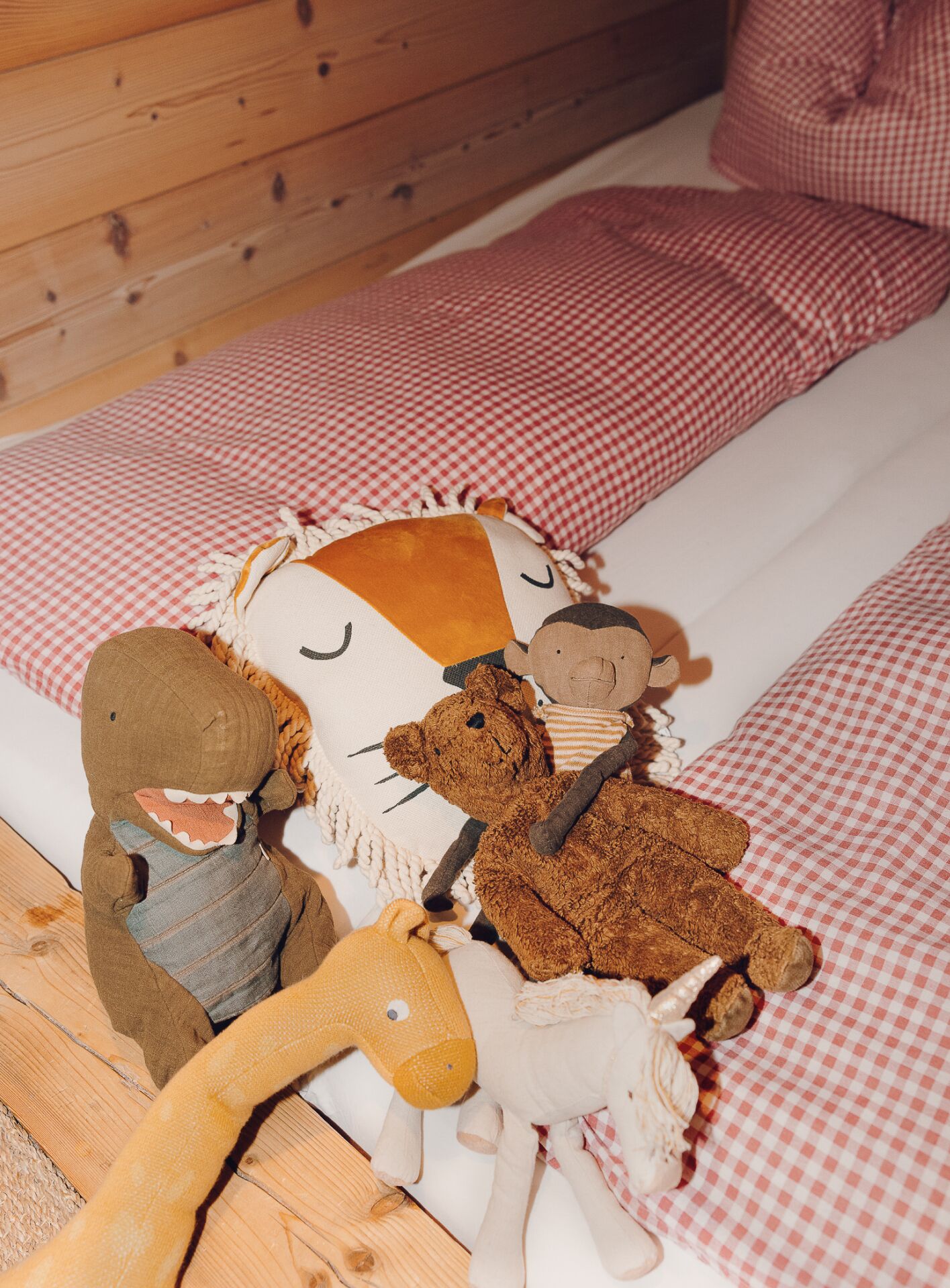 Una cama con una colcha a cuadros y almohadas, y varios peluches sobre la cama.