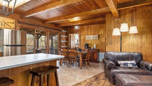 L’intérieur d’un chalet rustique comprend un coin repas en bois, un canapé en cuir et une cuisine équipée d’un réfrigérateur en acier inoxydable.