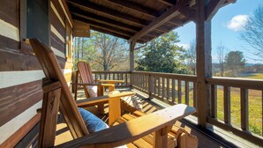 Une terrasse en bois avec des fauteuils Adirondack et une table en bois, offrant une vue sur un paysage pittoresque.