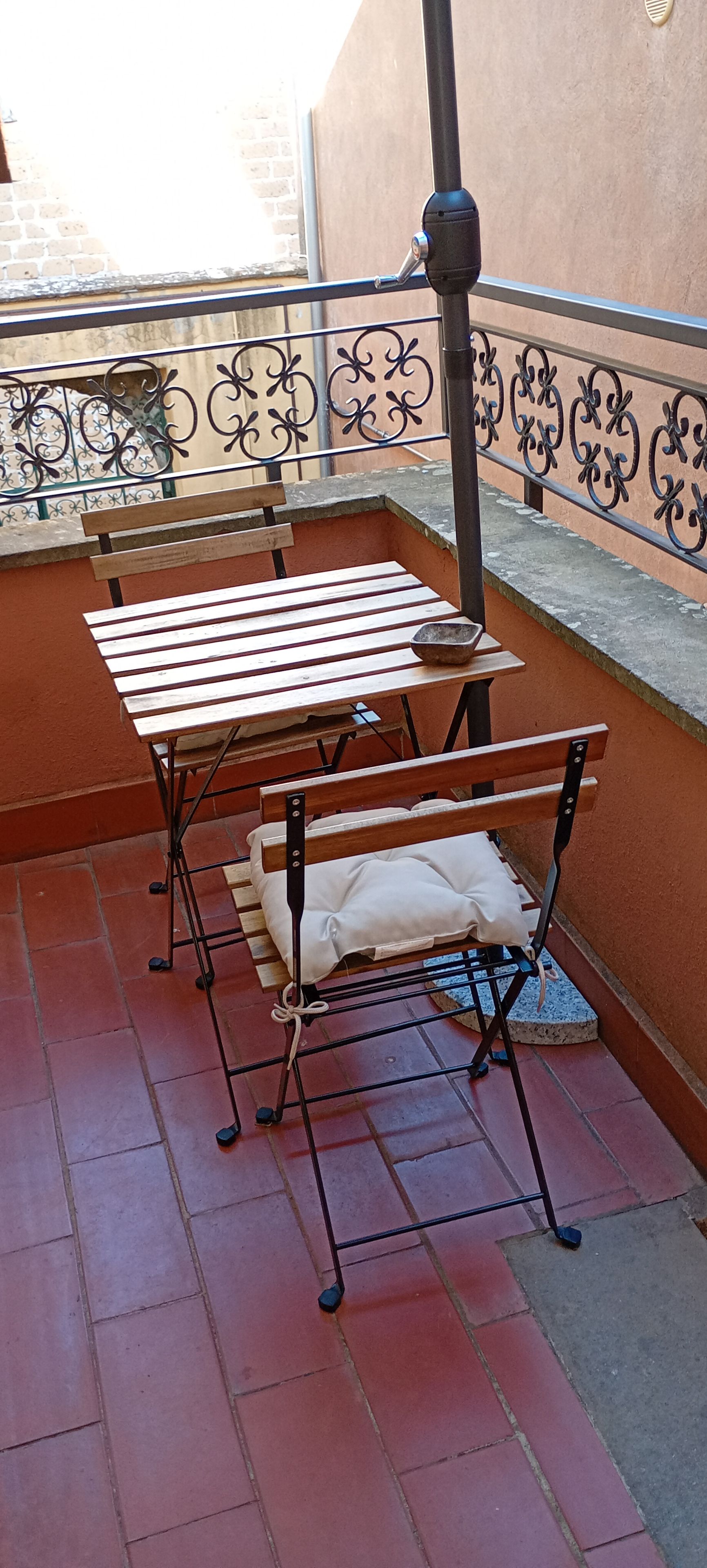A balcony with a metal table and bench, a small rug, and a decorative metal railing.