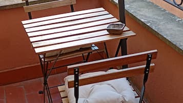 A balcony with a metal table and bench, a small rug, and a decorative metal railing.