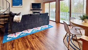 A spacious living room with a wooden ceiling, a large window, a sofa, a TV, and a staircase. - Bluebird Chalet - Spacious 3 bedroom + loft.  Storyland, North Conway, Jackson (Bartlett)