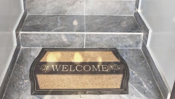 Eine Marmortreppe mit einer Fußmatte mit der Aufschrift 'WELCOME' am unteren Ende.
