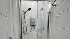 En duschkabin med glasväggar, ett handhållet duschmunstycke och en väggmonterad kontrollpanel.