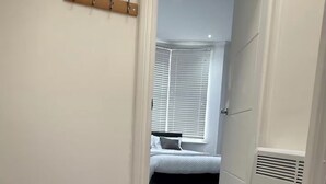 En smal hall som leder till ett sovrum med en säng, ett element och en klädställning.