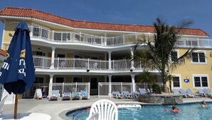 Un hotel con zona de piscina, varios balcones y sillones de descanso.